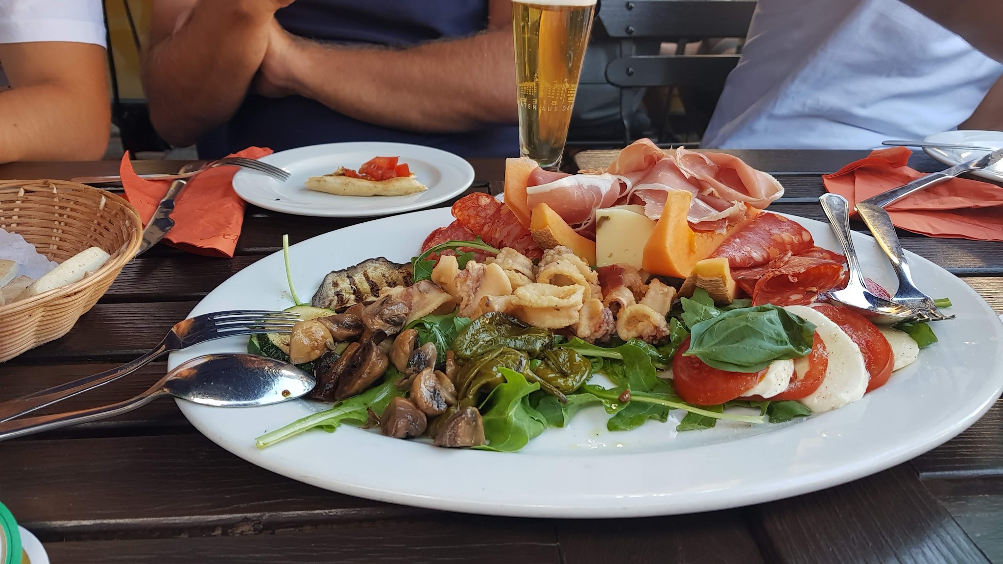 Antipasti-Teller mit Parmaschinken, Salami, Calamari, Mozzarella und Melone, dazu ein Paulaner Bier